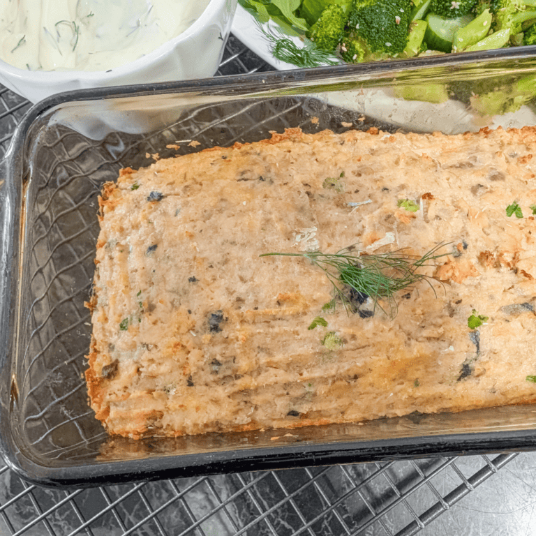 Baked salmon loaf garnished with herbs, served with broccoli and cucumbers.