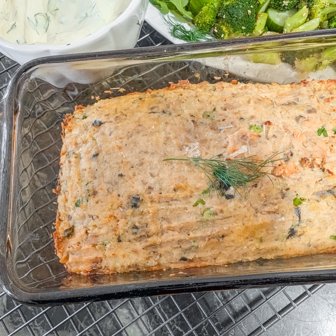 Baked salmon loaf garnished with herbs, served with broccoli and cucumbers.