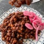 forkful of boston baked beans beans on plate with red pickled onion
