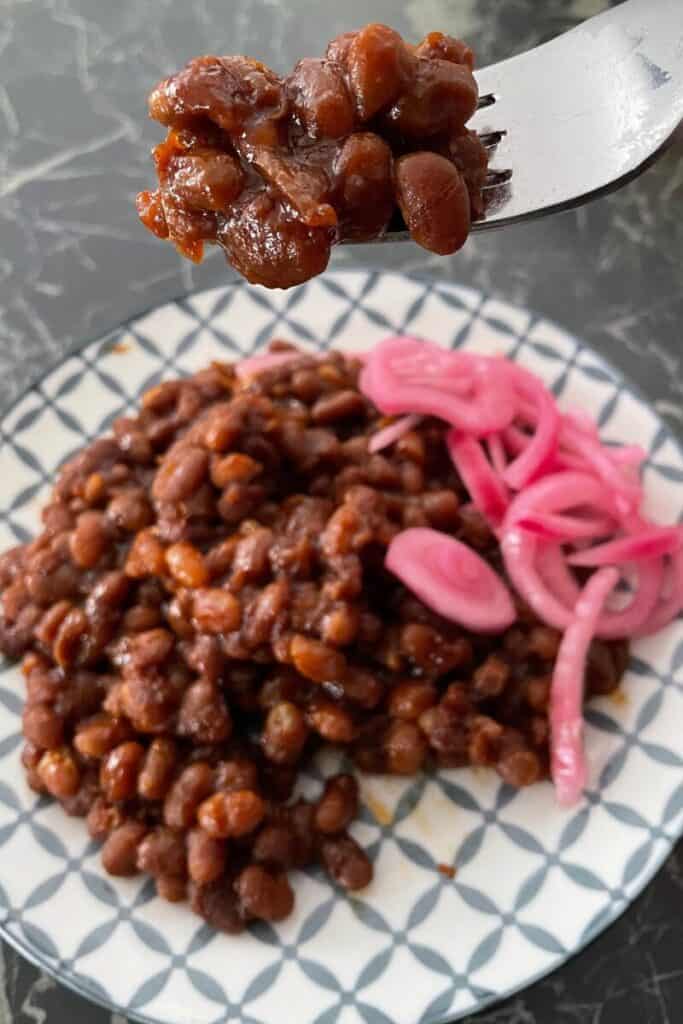 forkful of boston baked beans beans on plate with red pickled onion