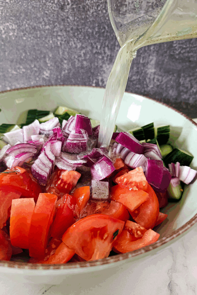 adding the lemon vinaigrette to the tomato cucumber salad