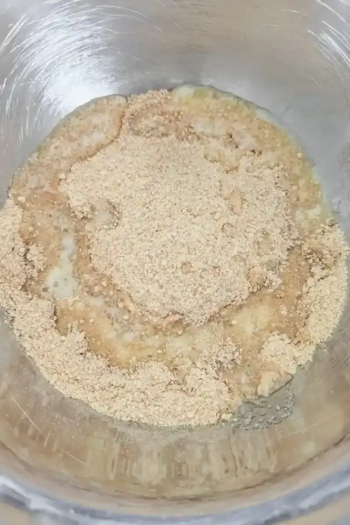 adding melted butter to graham cracker crumbs in stainless steel mixing bowl