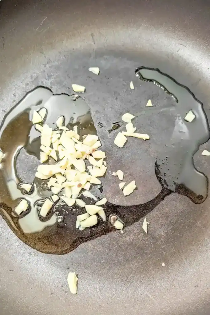 slivered garlic cloves in frying pan with olive oil