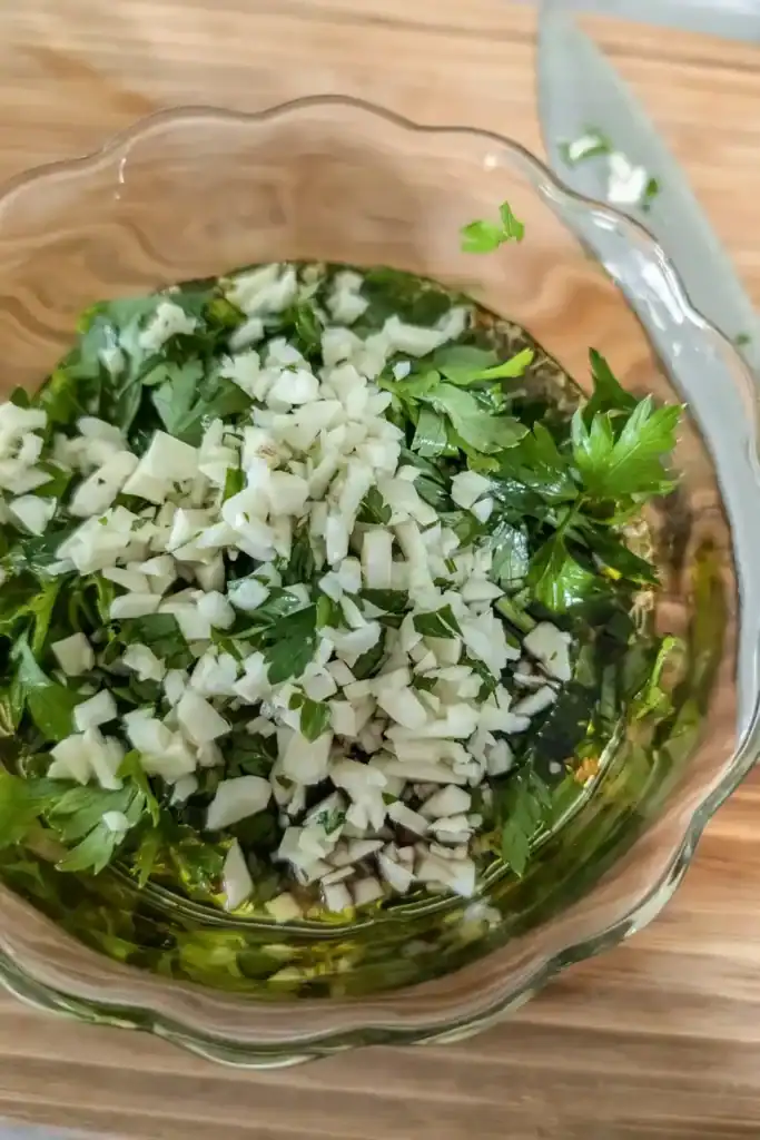 adding diced minced garlic to chimichurri sauce