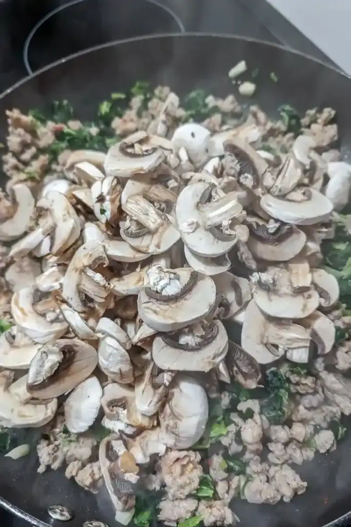 adding sliced mushrooms to sausage sauce