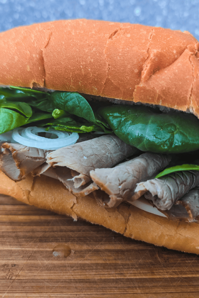 Close-up of a homemade roast beef sub sandwich with fresh greens and onions.