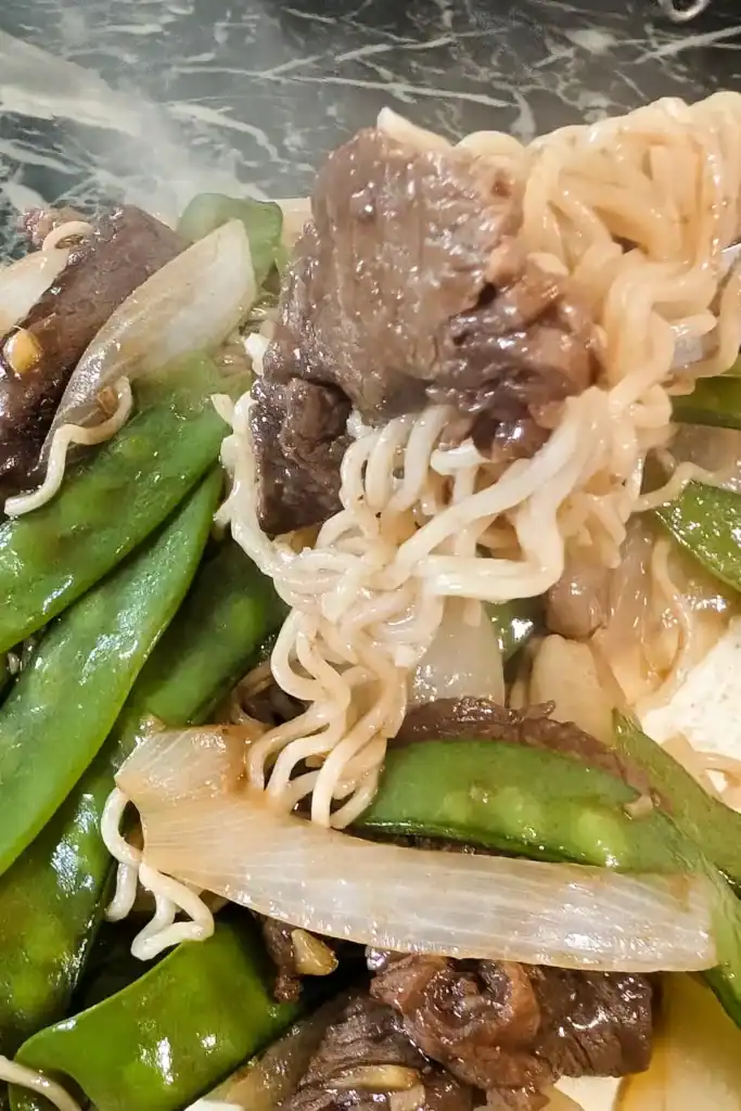 a close up forkful of beef and noodles from the ginger beef and snow pea noodle dish