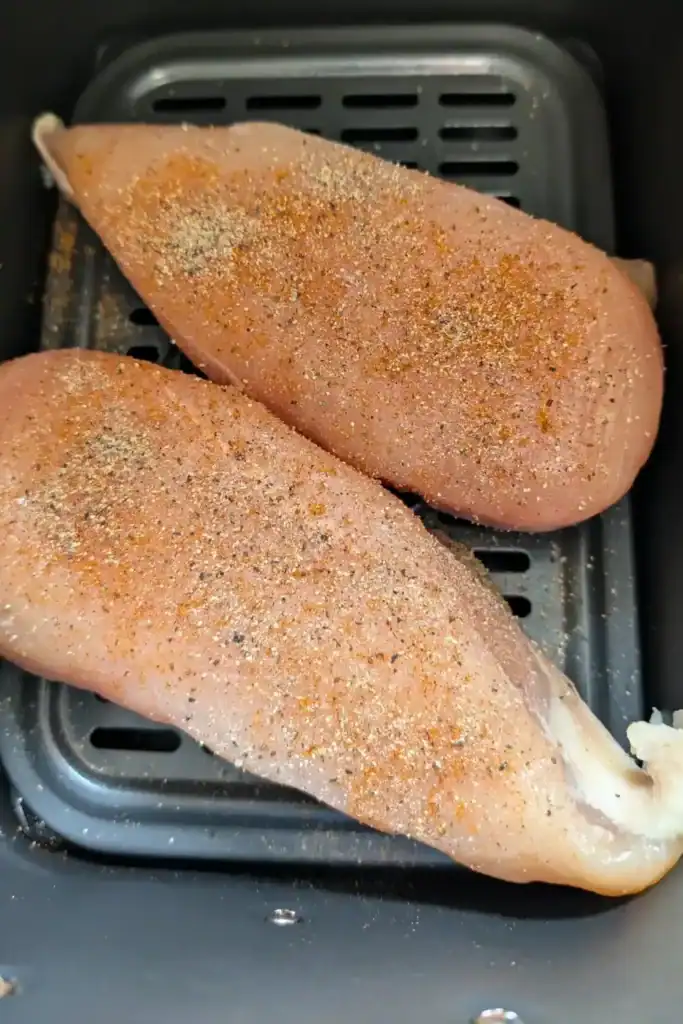 two boneless skinless chicken breast raw with old bay seasoning and black pepper in Ninja foodi air fryer