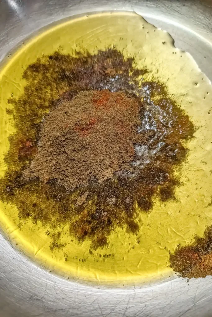 adding Indian spices to heated ghee in stainless steel saute pan