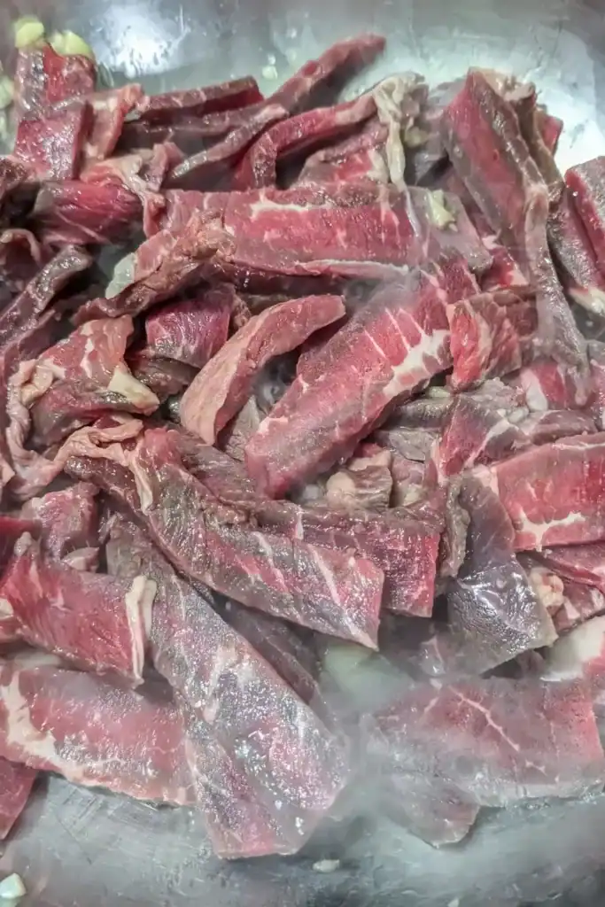 cooking the marinated beef strips with the aromatics in stainless steel bowl