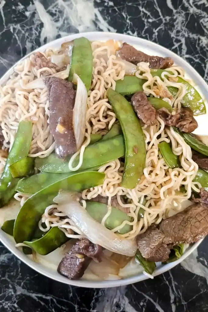 the plate of ginger beef and snow peas with noodles as seen from above