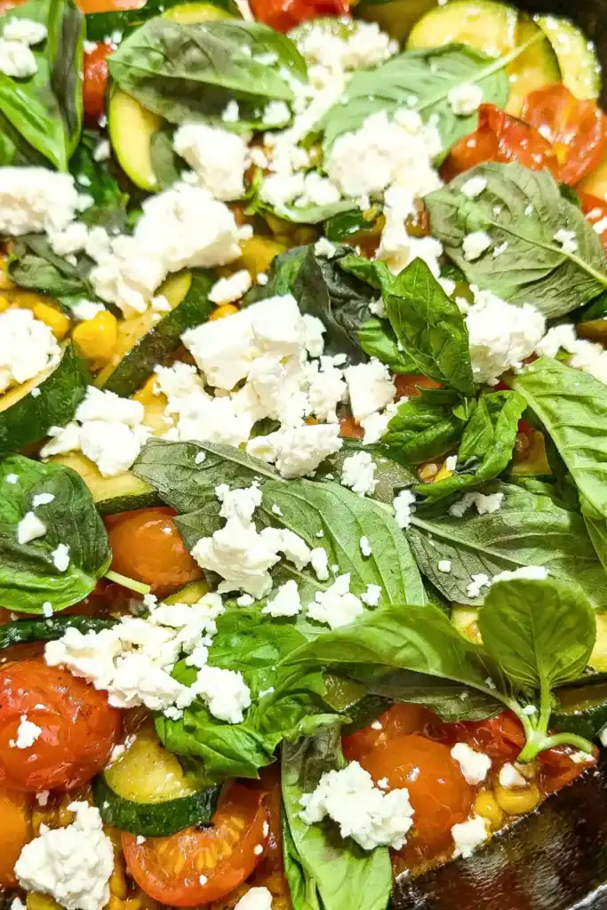 adding crumbled feta cheese to vegetable side dish in cast iron skillet