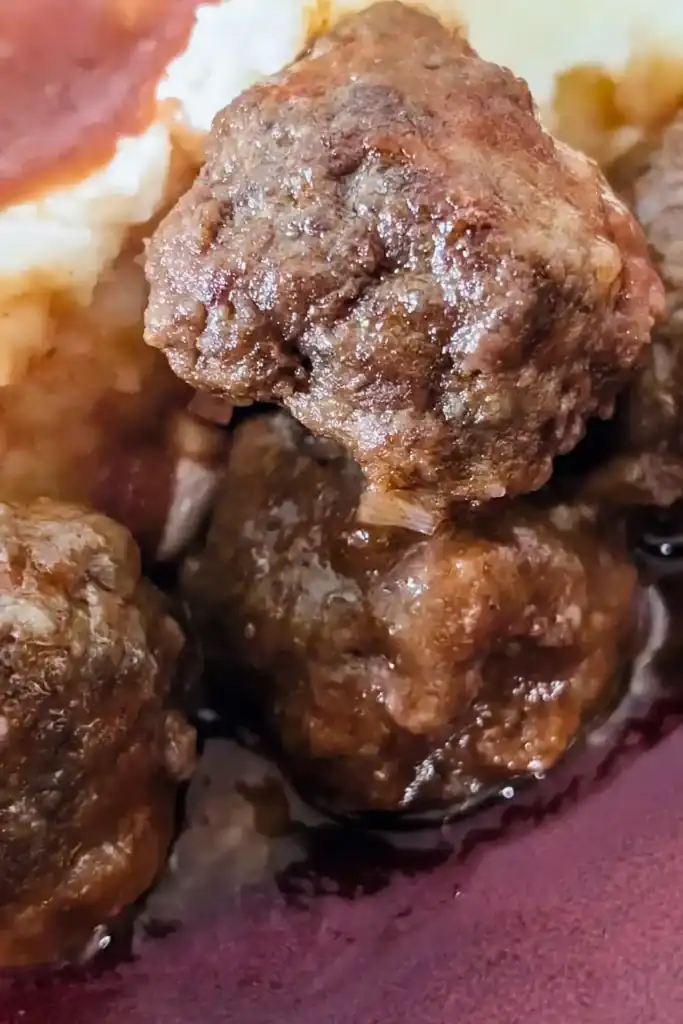 three bbq meatballs beside some mashed potatoes with sauce in back left corner