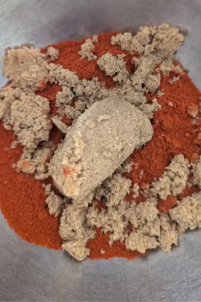 adding brown sugar to paprika for dry rub in stainless steel mixing bowl