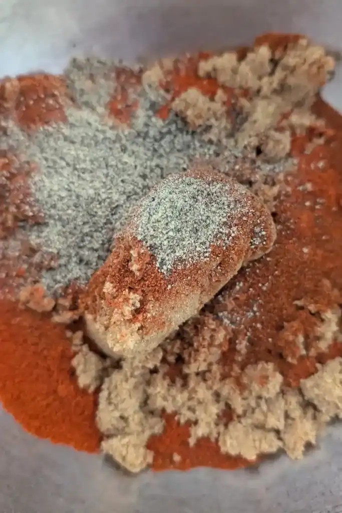 adding black pepper and garlic powder to dry rub in mixing bowl