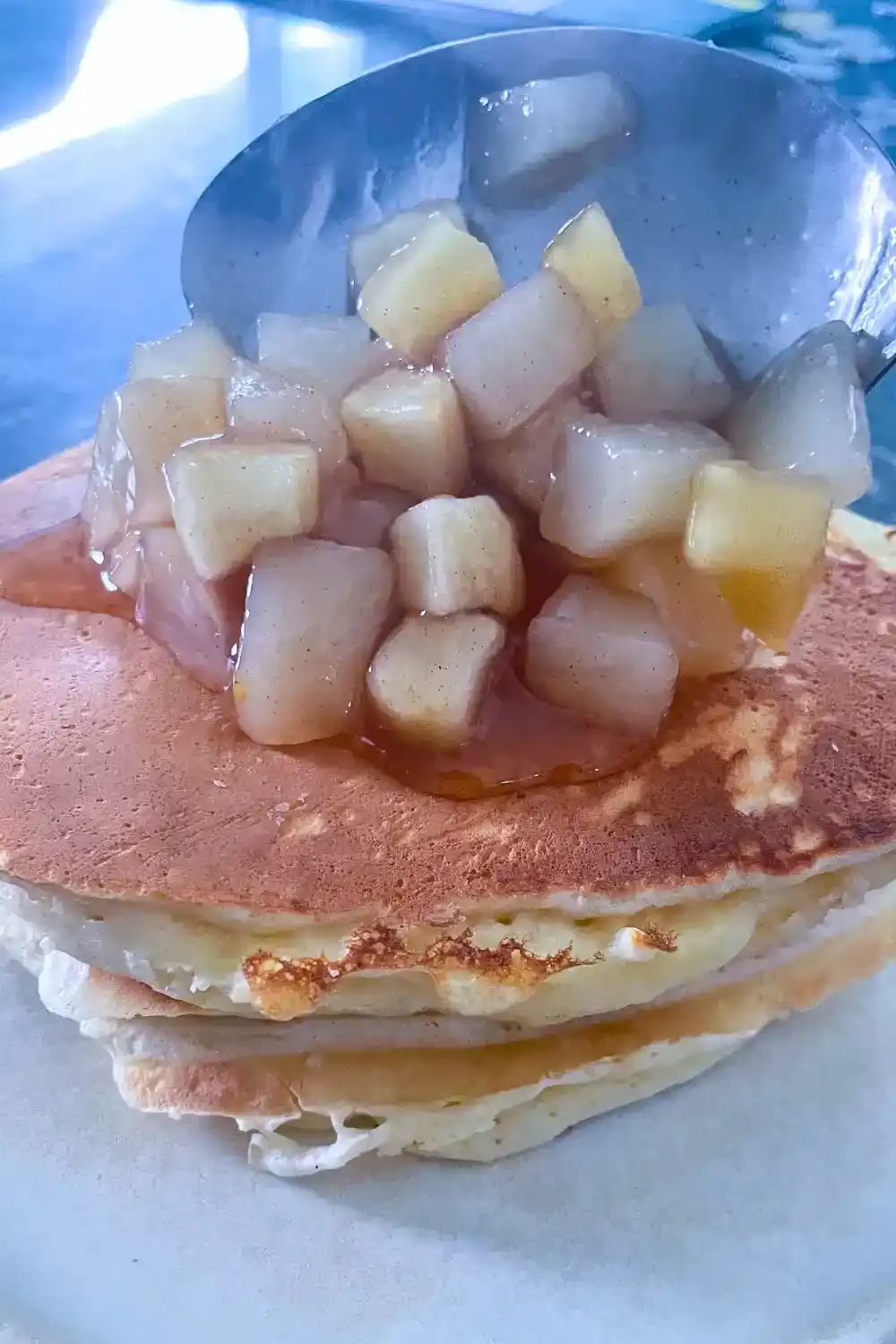 apple cinnamon pear compote being scooped over a stack of pancakes