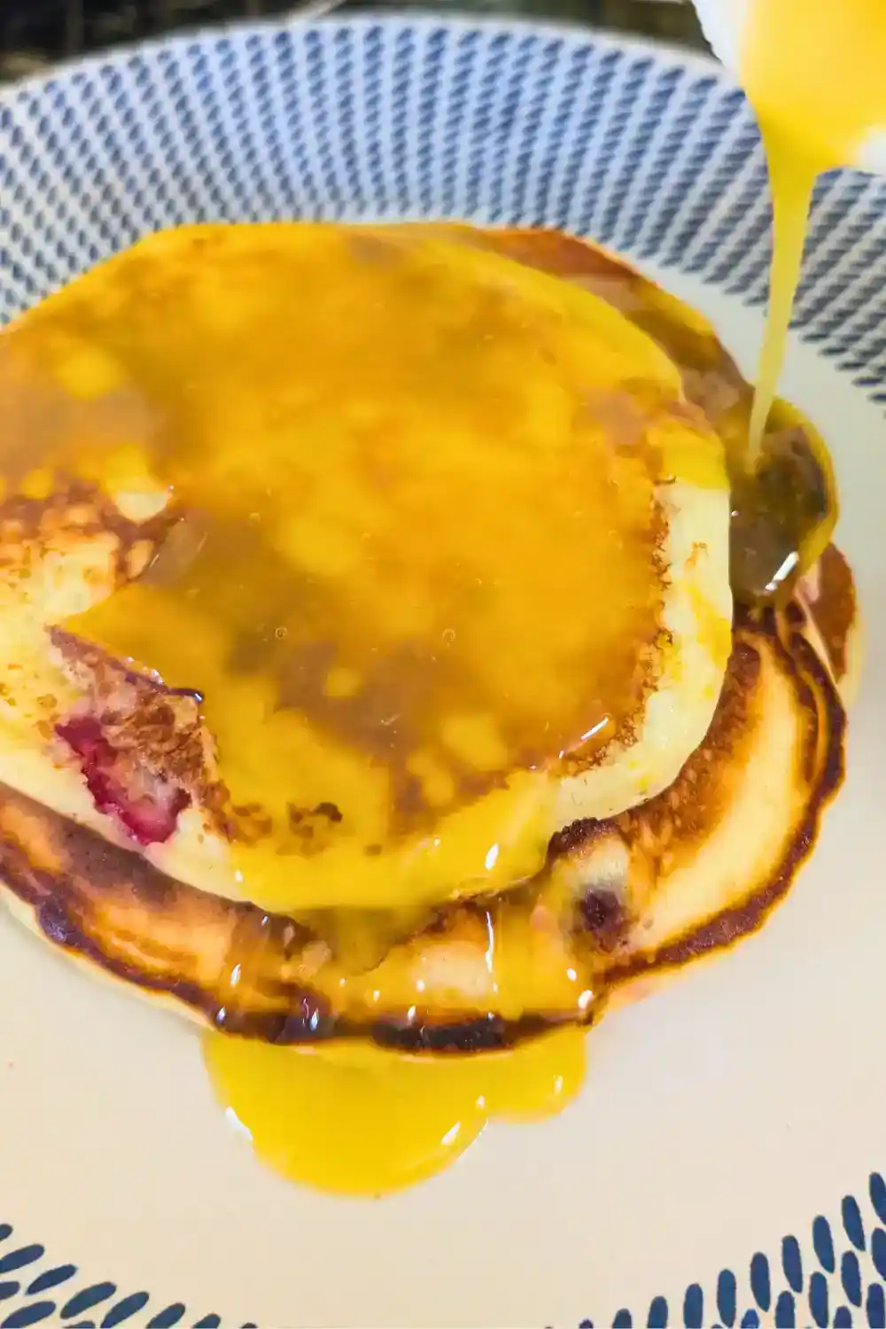 drowning orange cranberry pancakes on blue and white plate with orange sauce