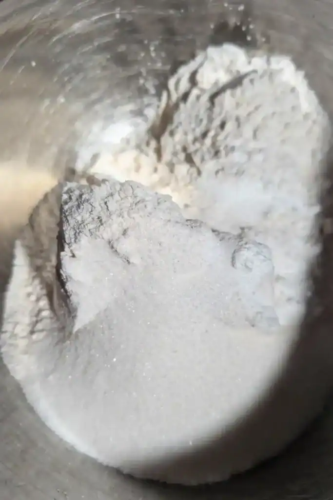 adding baking powder salt sugar to flour in mixing bowl