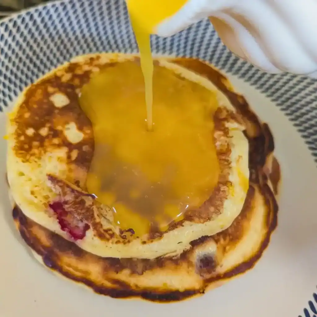 pouring orange sauce over the cranberry orange pancakes
