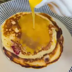 pouring orange sauce over the cranberry orange pancakes