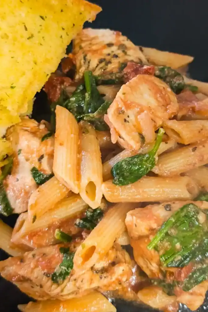 the rose sauced chicken penne pasta on black plate with a side of garlic bread