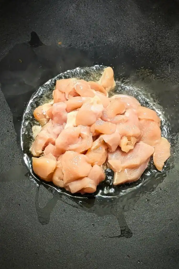 chopped boneless skinless chicken breast in hot wok with oil