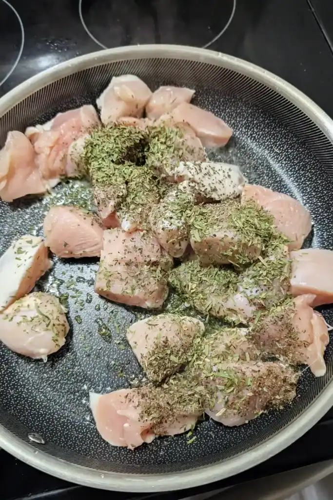 adding dry savory and basil to chicken breast pieces in frying pan
