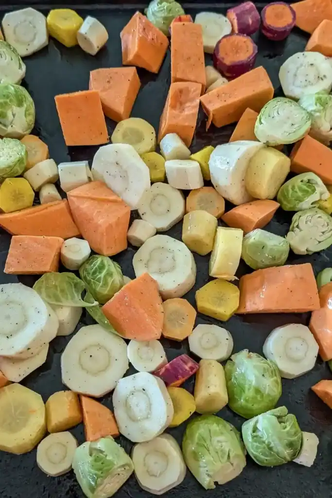 single layer of seasoned vegetables on black baking sheet