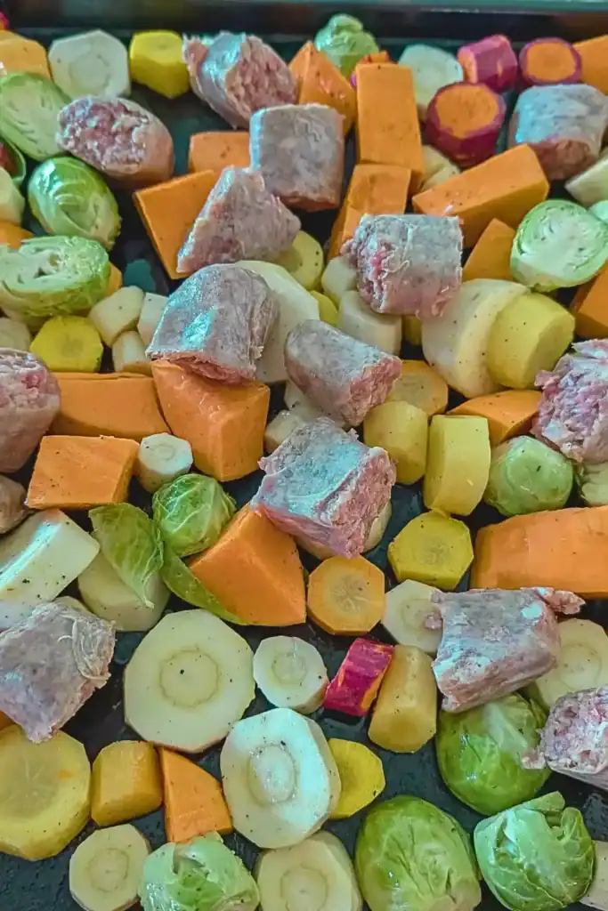 adding cut up Irish bangers to the vegetables on baking sheet