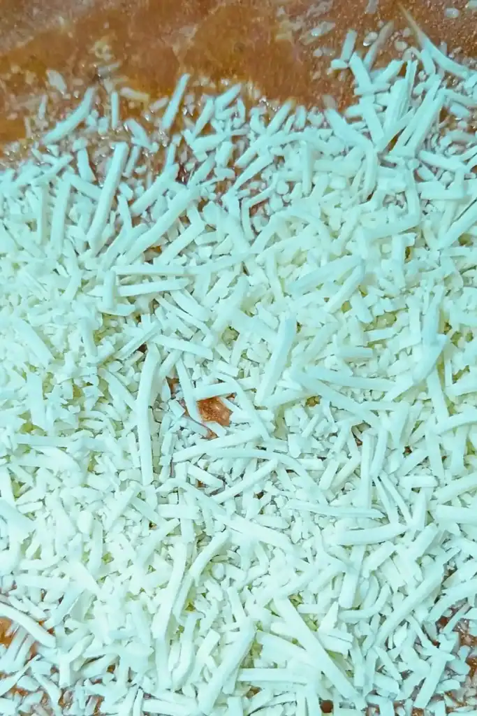 adding shredded fresh parmesan cheese to rose sauce in frying pan