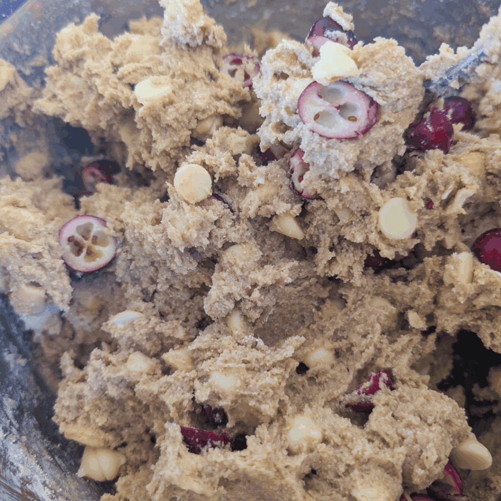 Creamy cookie dough with white chocolate chips and pomegranate seeds for delicious baking or snacking.