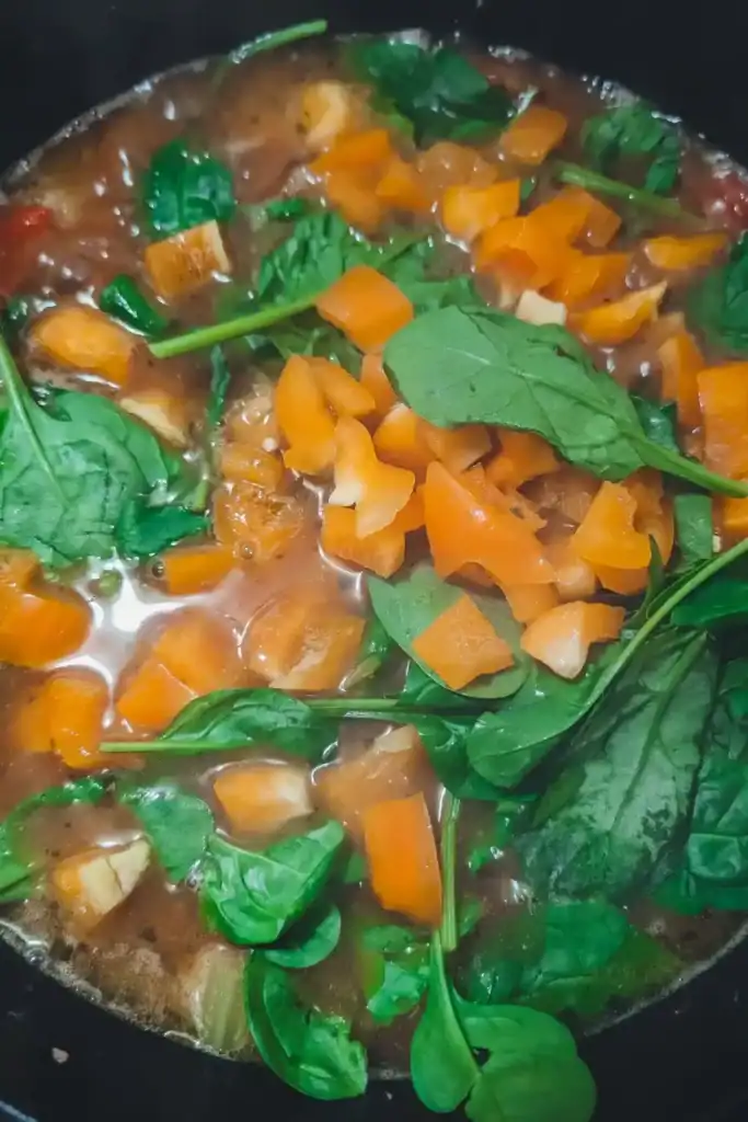 adding the yellow bell pepper and baby spinach to the hamburger soup