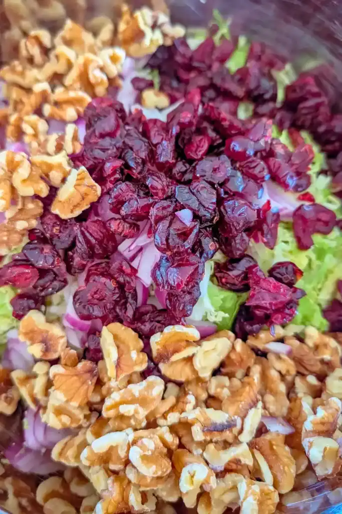 adding walnuts to brussels sprout raw salad in bowl