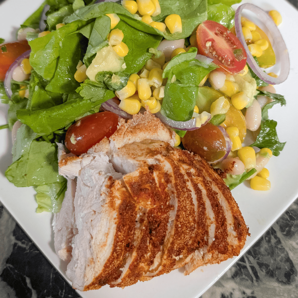 Grilled chicken salad with chipotle dressing, fresh vegetables, and corn on a white plate.