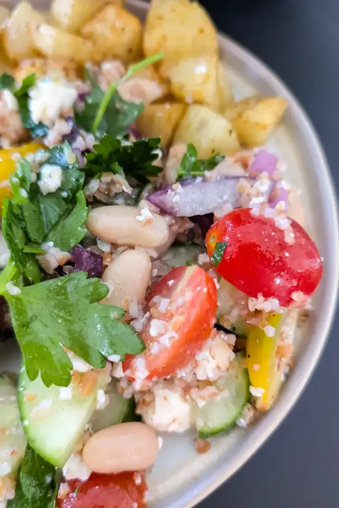 serving salad on edge of round plate with potato in behind