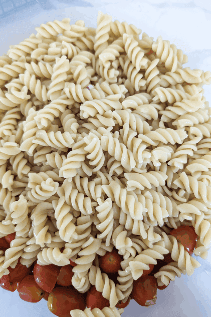 adding cooked and cooled rotini pasta to salad bowl