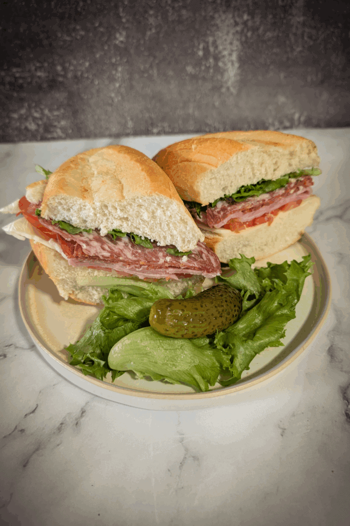 cut in half the sub served with dill pickle on a bed of lettuce on round beige plate
