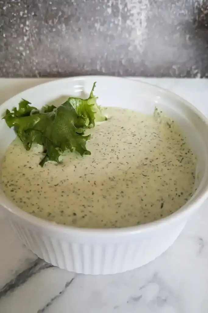 green goddess herbed dressing in fluted white bowl with a green lettuce leaf
