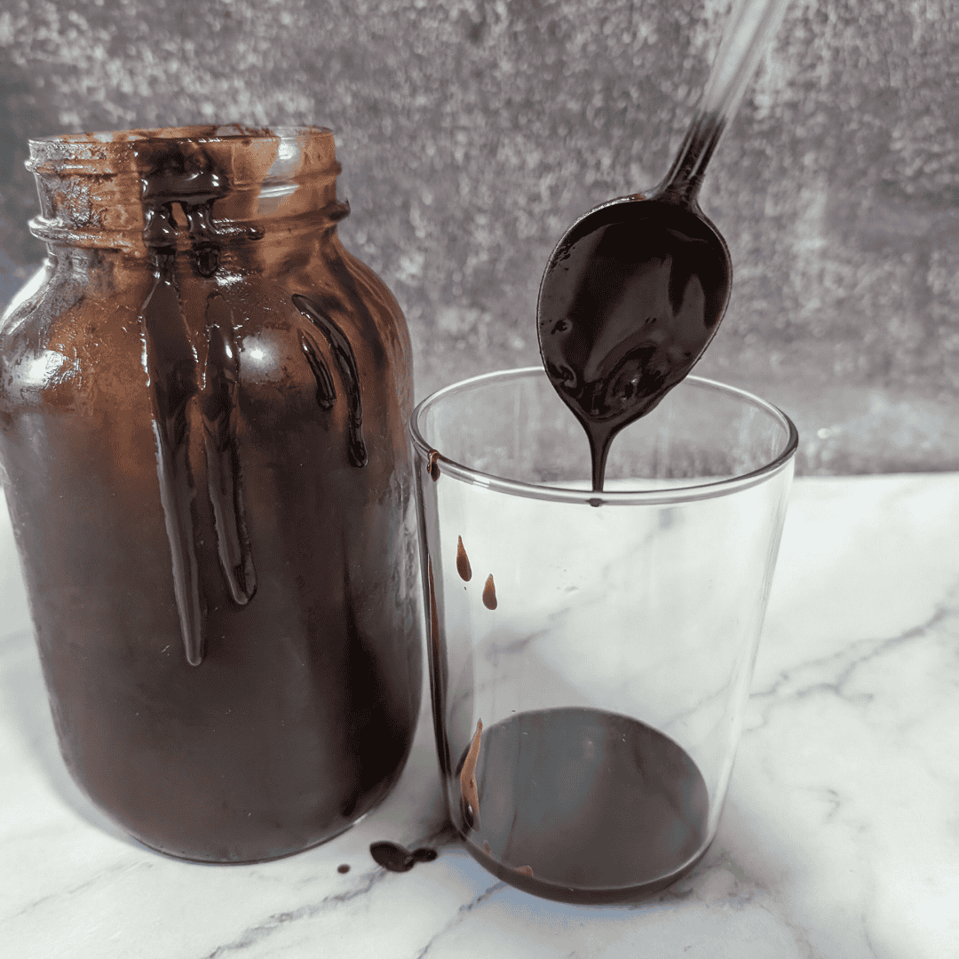 A spoon being poured into a glass of chocolate syrup.
