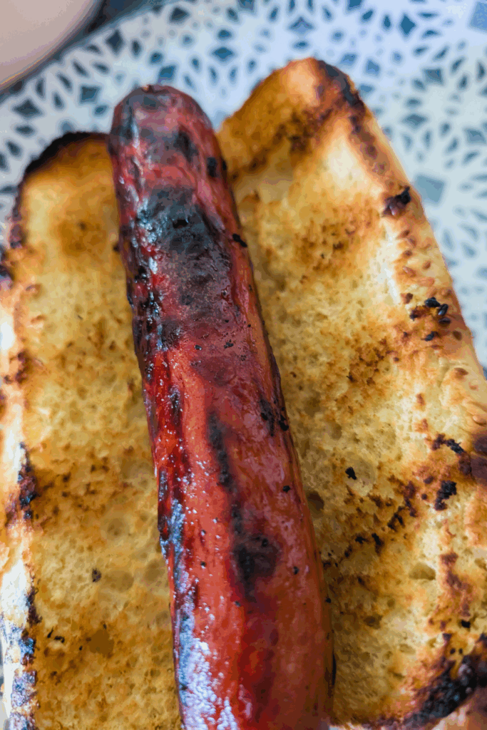 adding the cooked hot dog to the toasted bun on blue and white plate