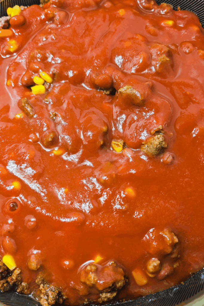 adding the tomato sauce to chili meat mixture