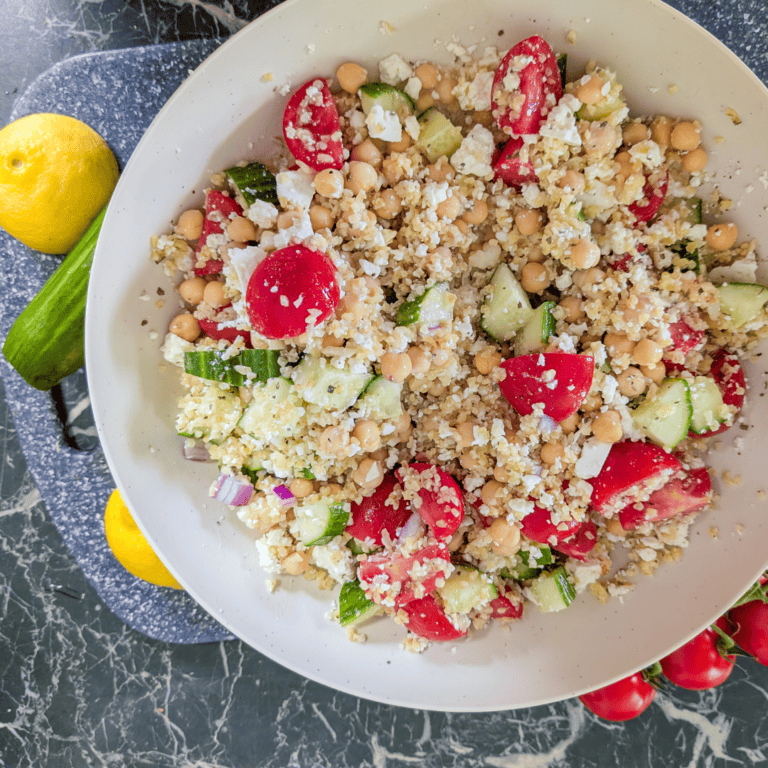 Colorful chickpea and tomato salad with cucumber, feta, and herbs on a white plate.