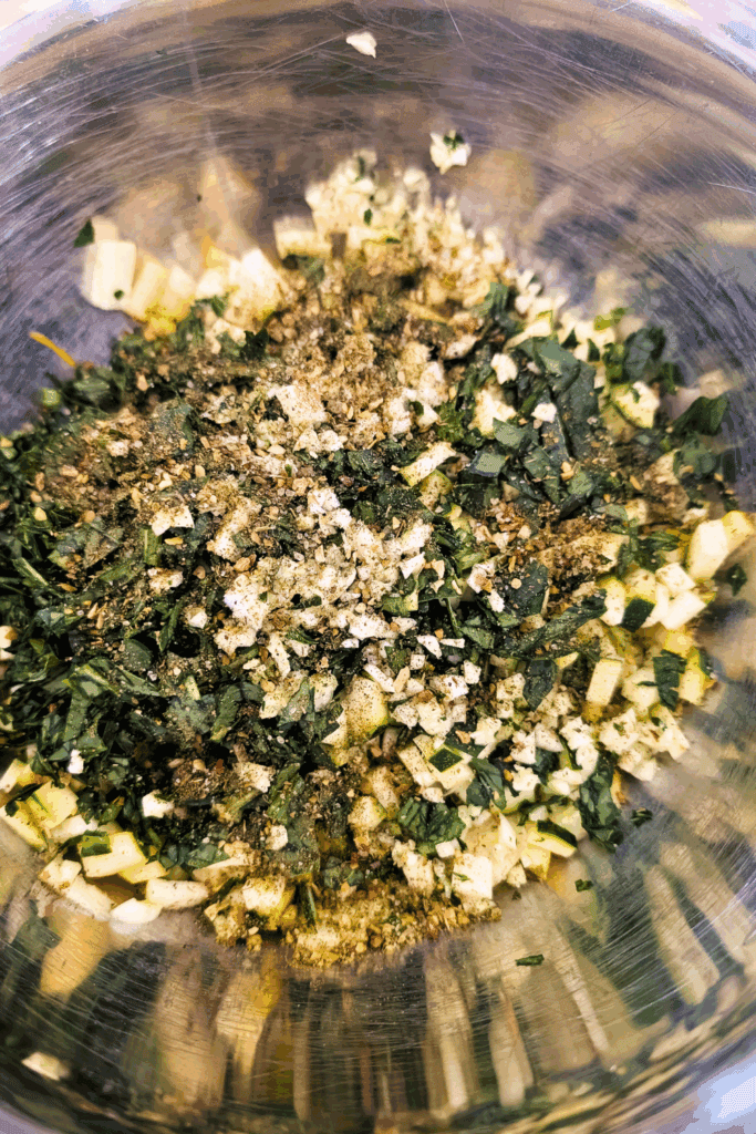 Diced vegetables with herbs and spices in a mixing bowl.