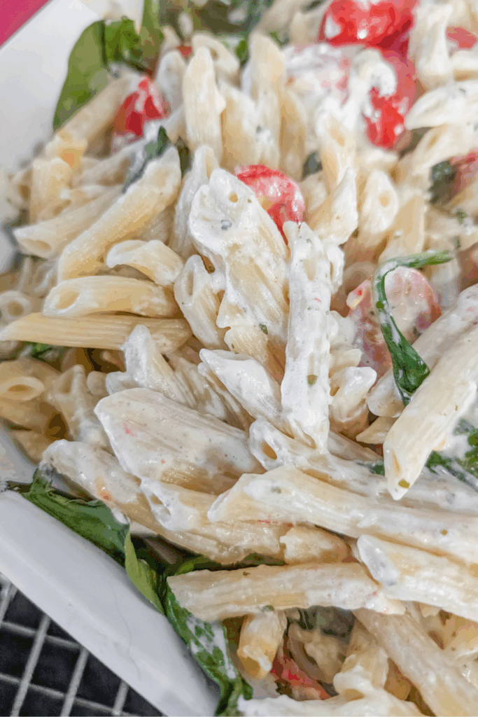 Creamy pasta salad with cherry tomatoes and fresh spinach, perfect for summer meals.