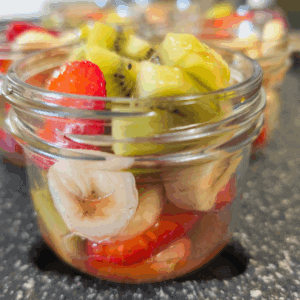 Fresh fruit salad in glass jar with strawberries, bananas, kiwi, and other mixed fruits, healthy homemade snack or dessert, vibrant colorful fruit mix.