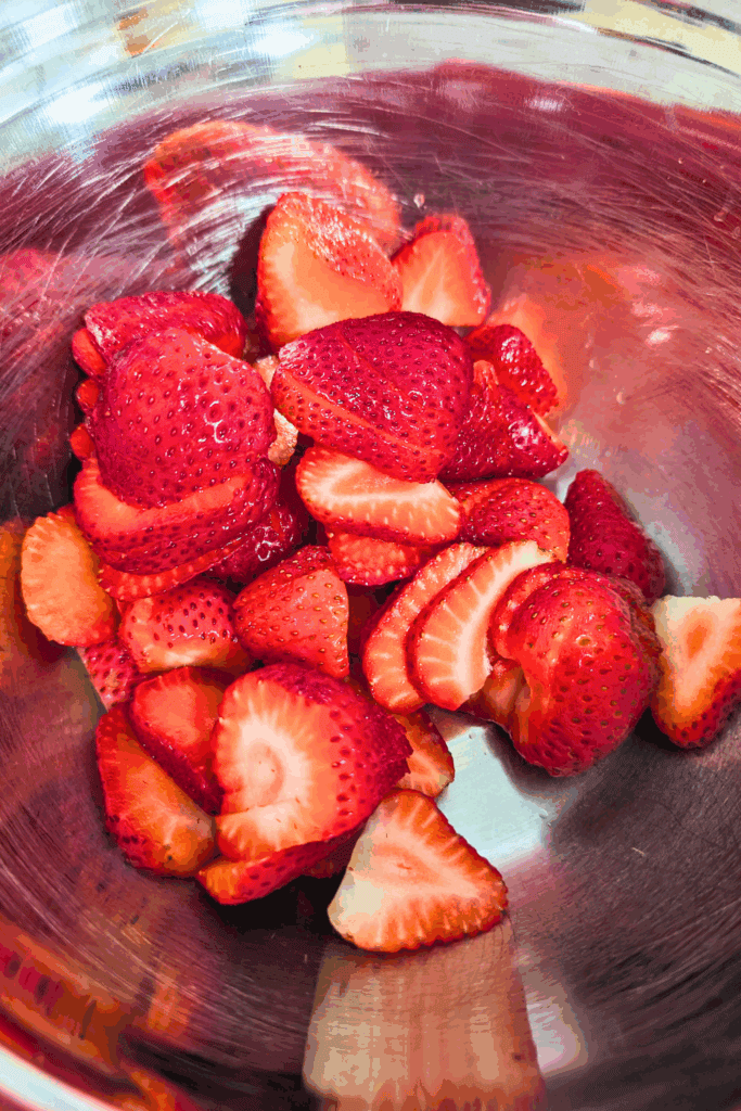 Fresh sliced strawberries in a stainless steel mixing bowl for healthy dessert recipes.
