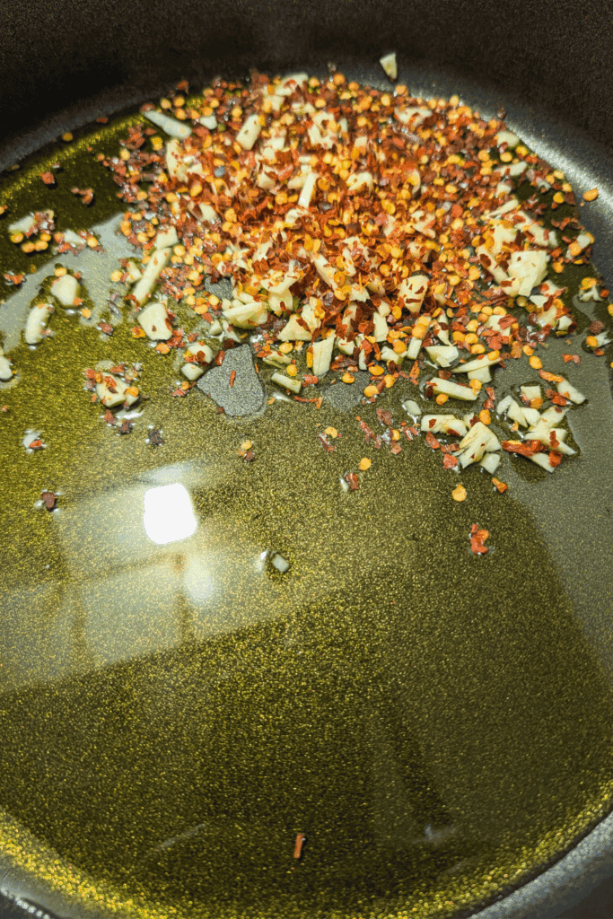 Olive oil with minced garlic and crushed red pepper flakes cooking in a pan.