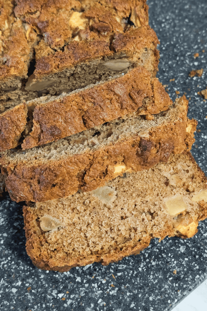 Close-up of freshly baked banana bread with nuts, sliced on a textured black surface.