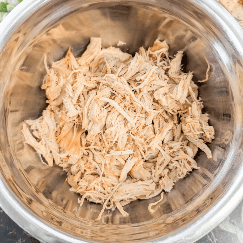 Shredded chicken breast in a stainless steel bowl, perfect for easy meal prep in Dutch oven recipes.