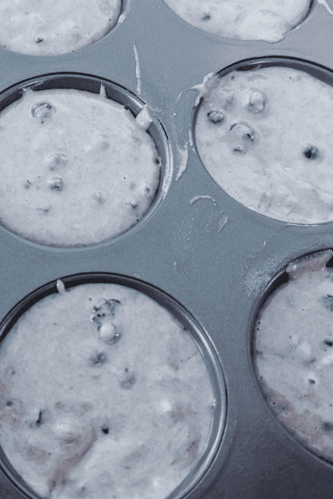Fresh wild blueberry muffin batter in a muffin tin with frozen Canadian wild blueberries.